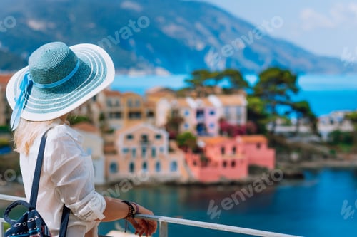 Preview: Tourist woman in blue sunhat and white clothes enjoying top view of colorful tranquil village Assos