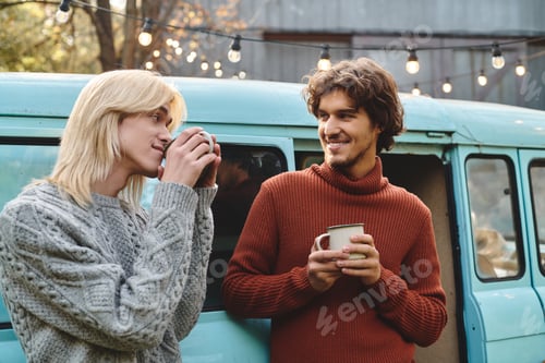 Preview: Two young friends enjoying warm drinks together by a vintage van in a cozy outdoor setting