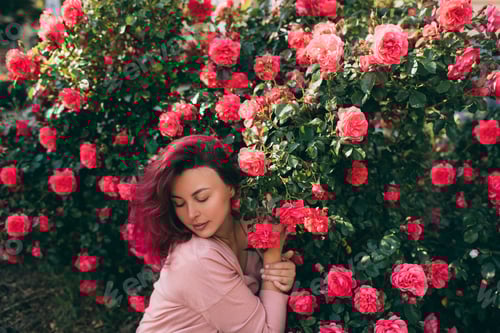 Preview: Beautiful woman with bright pink hair enjoying rose fragrance in a spring garden