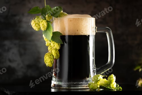 Preview: Glass of dark beer with hops around on a dark background