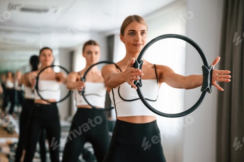 Preview: Standing, smiling, holding circle in hands. Women in fitness center are doing exercises