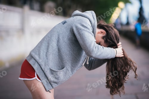 Vista previa: Young female runner tying up long hair on riverside