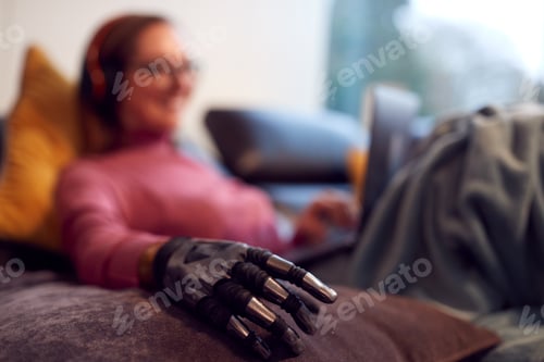 Preview: Woman With Prosthetic Arm Wearing Wireless Headphones And Working On Laptop On Sofa At Home