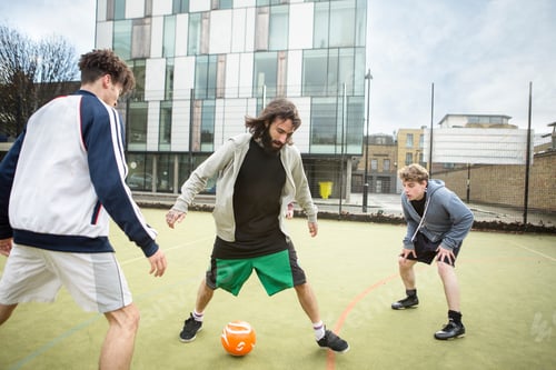 Preview: Group of adults playing football on urban football pitch