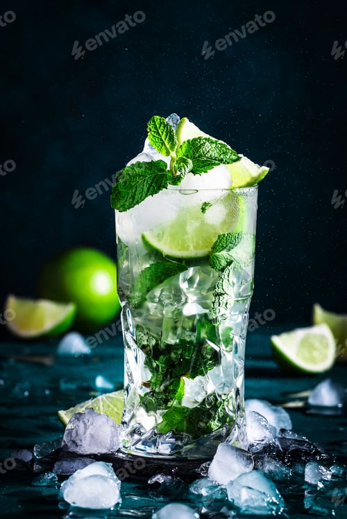 Preview: Mojito cocktail with lime, white rum, soda, cane sugar, mint, and ice in glass on deep blue .
