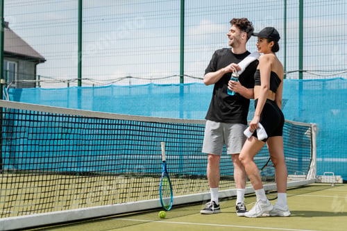 Preview: happy couple standing with towel and sports bottle near tennis net, racket and ball on court
