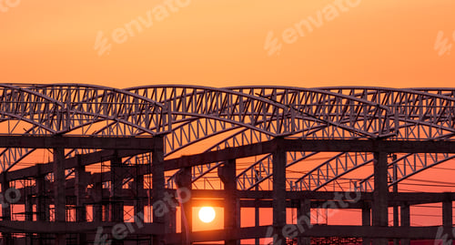 Preview: Silhouette curve metal roof beam outline on industrial building structure against orange sunset sky