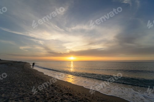 Preview: An individual strolls along the shore in the early morning, as the sun ascends over the horizon.