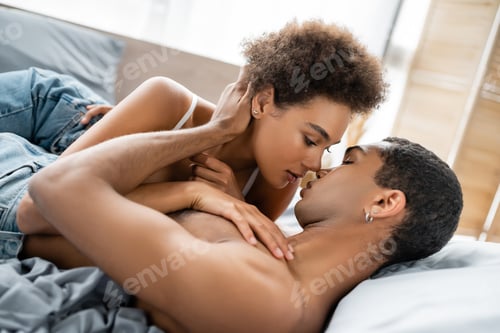 Preview: young and passionate african american couple hugging and looking at each on bed at home