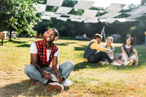 Preview: selective focus of african american man in headphones with notebook resting on green grass with