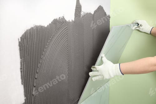 Preview: Worker installing ceramic tile on wall, closeup. Space for text