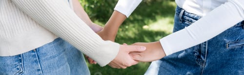 Preview: cropped view of women in jeans holding hands outside, banner