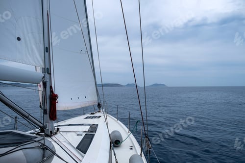 Preview: Sailing in Aegean sea, Greece. Sailboat with open white sail, cloudy sky and rippled sea.