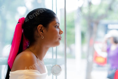 Preview: Young woman looking through window in coffee shop