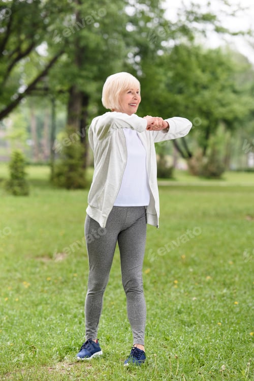 Preview: senior caucasian sportswoman exercising on green lawn in park
