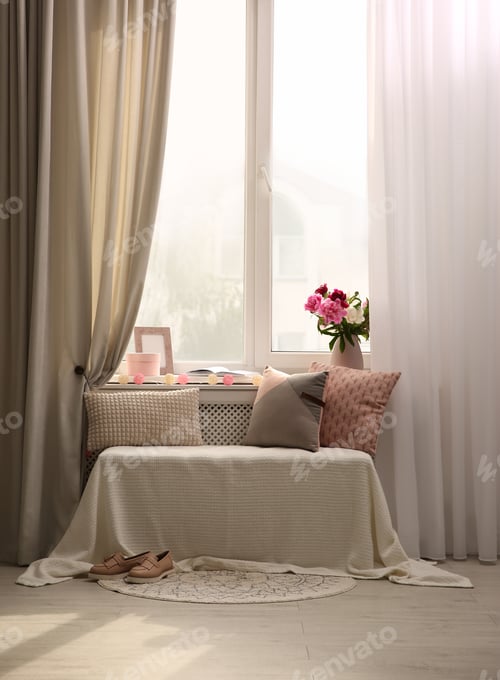 Preview: Comfortable place for rest with cushions and peony flowers near window indoors