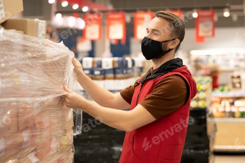 Preview: Young male worker of supermarket unpacking huge stack of packed boxes with goods