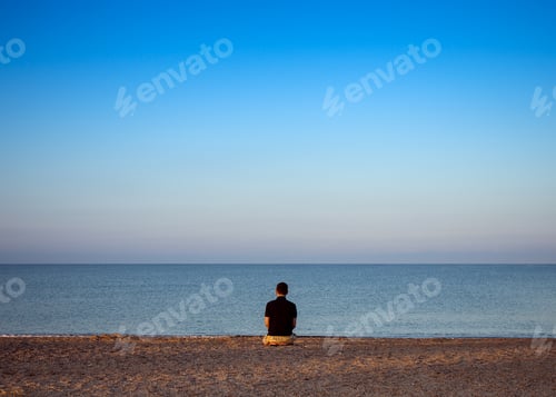 Preview: A young man meditates on the beach during sunset.