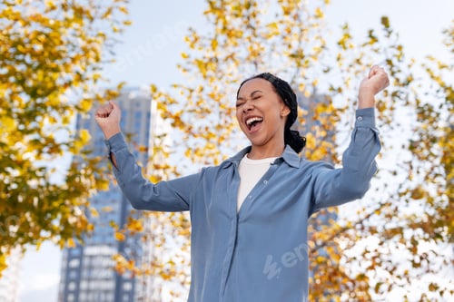Preview: Happy young African American woman celebrating triumph and success outdoors