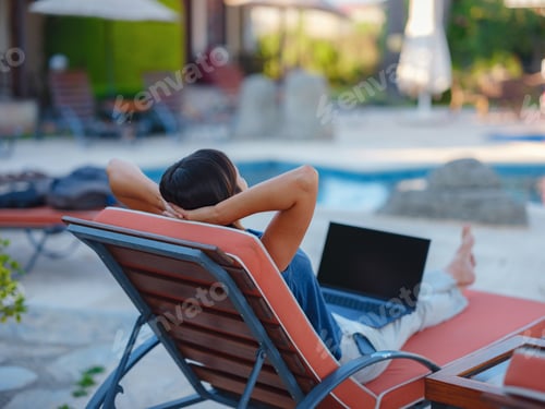 Preview: Young business woman working at computer by hotel pool.