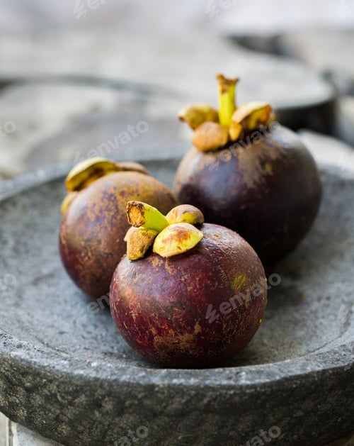 Preview: Vertical selective closeup shot of mangosteens on a gray surface