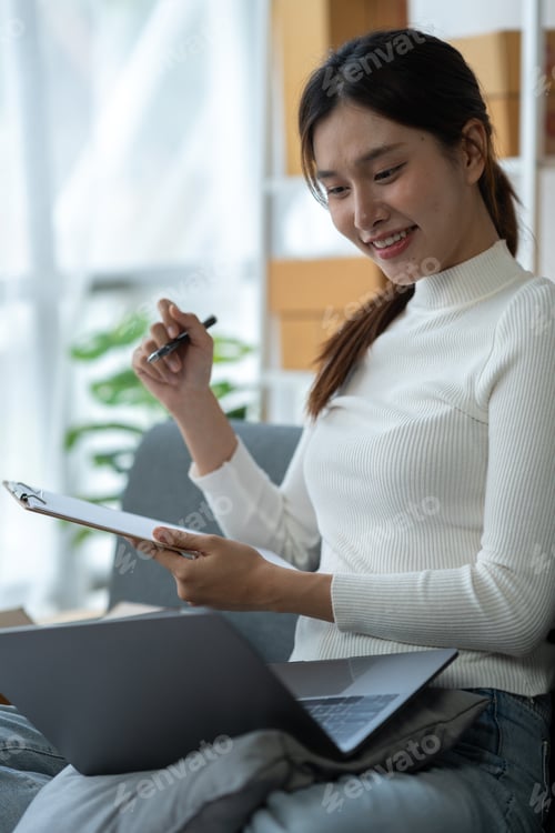 Preview: Asian businesswoman taking orders and checking online from laptop and mobile phone to prepare mercha