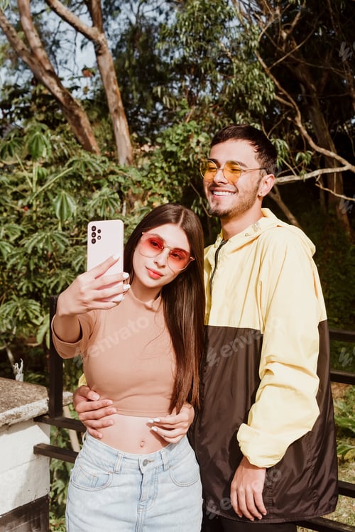 Preview: Couple of cool friends taking a selfie with their cell phone in the open air