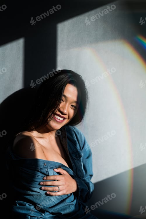 Preview: Young Asian female in denim shirt posing sensually and taking off denim shirt while smiling at
