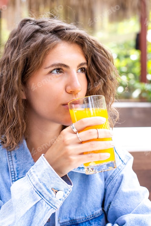 Preview: Beautiful young woman drinking healthy orange juice at outdoor cafe