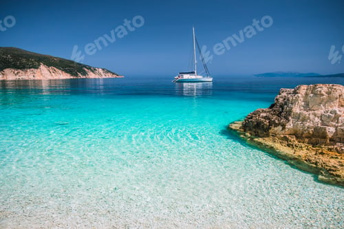 Preview: Beautiful azure blue lagoon with sailing catamaran yacht boat at anchor. Pure white pebble beach