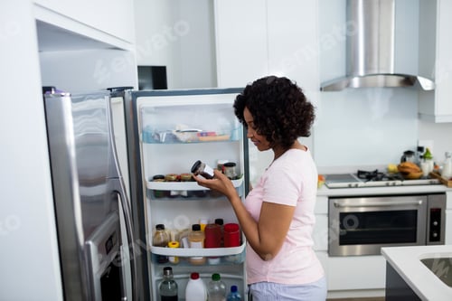 Preview: Woman removing bottle from refrigerator in kitchen
