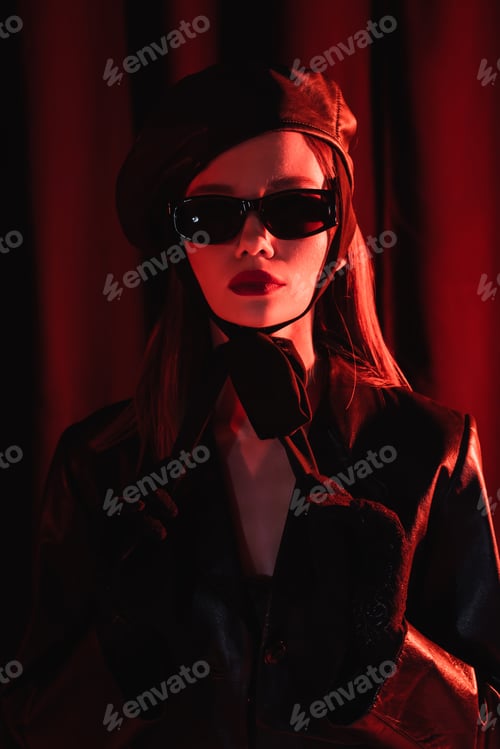 Preview: glamour woman in leather beret, black jacket, sunglasses and gloves posing on dark draped background