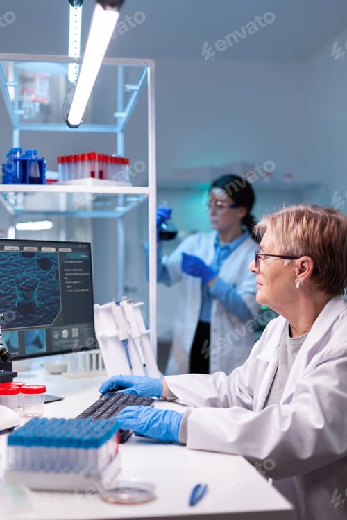 Preview: Senior doctor in white coat working on computer in discovery laboratory