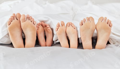 Preview: Eight feet resting in love. Shot of a family laying barefoot on a bed at home.
