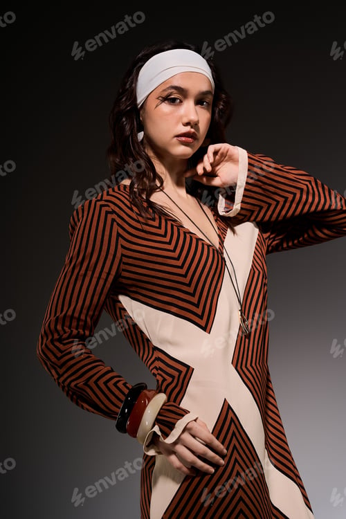 Preview: Stylish young woman in a striped dress posing gracefully in a modern studio setting