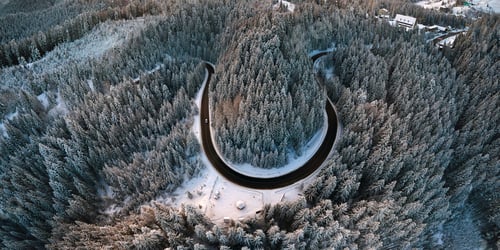 Preview: Aerial view of winter landscape with snow covered mountain hills and winding forest road in morning.