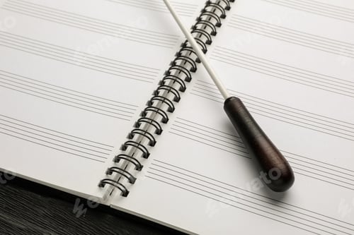 Preview: Conductor's baton and lead sheet on black wooden table