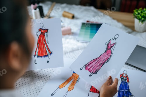 Preview: Young fashion designer looking on clothes sketch in hand