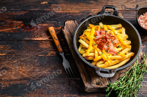 Preview: French fries with melted mix of cheddar cheese and bacon served in a pan. Dark wooden background