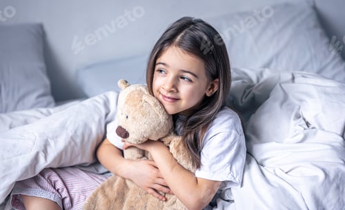 Preview: Sleepy little girl with her favorite teddy bear in bed in the morning.