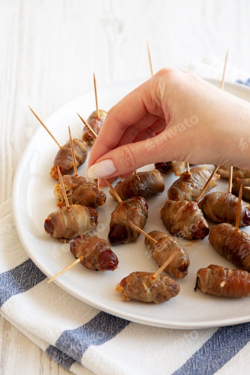 Preview: A woman's hand takes Bacon Wrapped Date, side view.