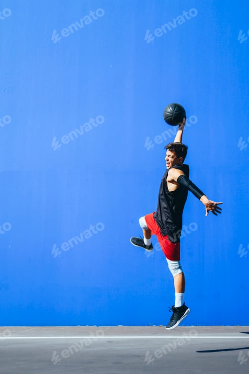 Preview: Man playing basketball in front of a blue wall.