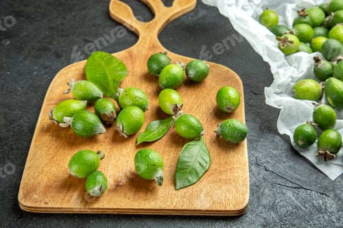 Preview: Close up view of natural fresh green feijoas on wooden cutting board and white page on dark