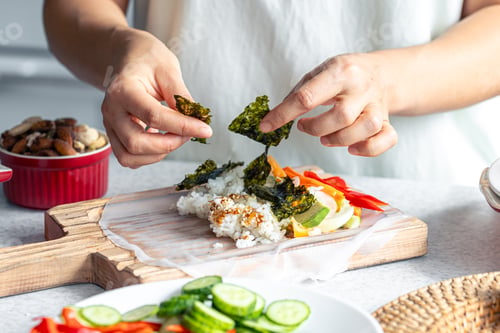 Preview: Woman preparing spring rolls in rice paper on kitchen table.