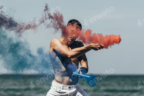 Preview: attractive shirtless man dancing with red and blue smoke sticks in front of ocean view