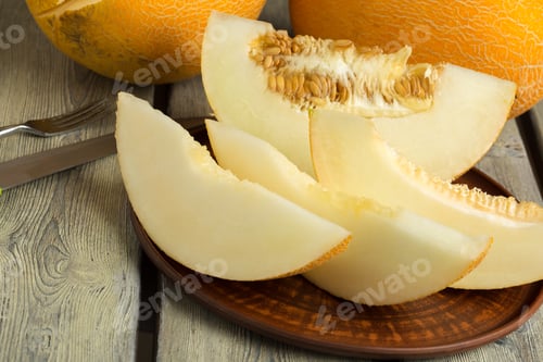 Preview: Fresh slices of melon on a wooden plate during a sunny day in a kitchen
