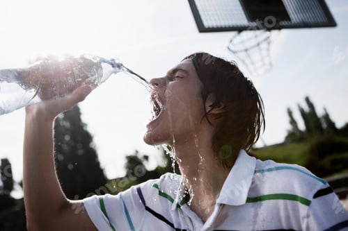 Preview: Germany, Berlin, Teenage boy pouring bottled water on face