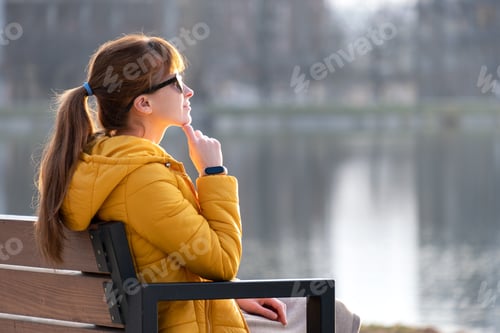Preview: Young woman sitting on park bench relaxing on warm spring day