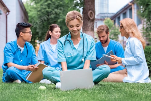 Preview: teacher and multiethnic students studying outdoors with gadgets at medical university