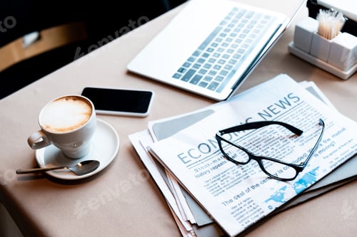 Preview: laptop and smartphone with blank screen, cup of coffee, documents, newspaper and glasses on table in